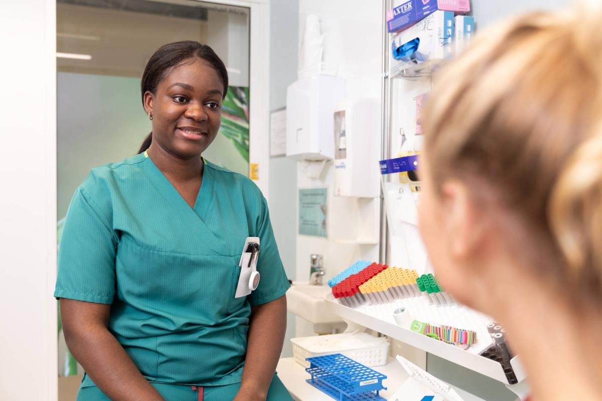 A laboratory nurse discussing with a patient. The patient is partly visible from behind. 