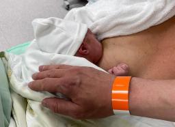 Tukihenkilö ja vastasyntynyt ihokontaktissa, kuvassa myös tukihenkilön ranneke.